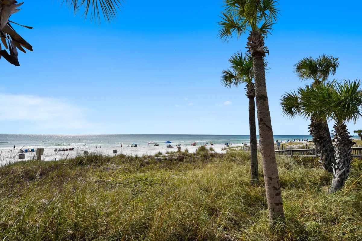 A lively beachfront scene featuring families and children playing on the sandy shore, palm trees swaying in the breeze, and the ocean stretching into the horizon. The atmosphere is cheerful, with activities such as sunbathing, swimming, and building sandcastles evident.