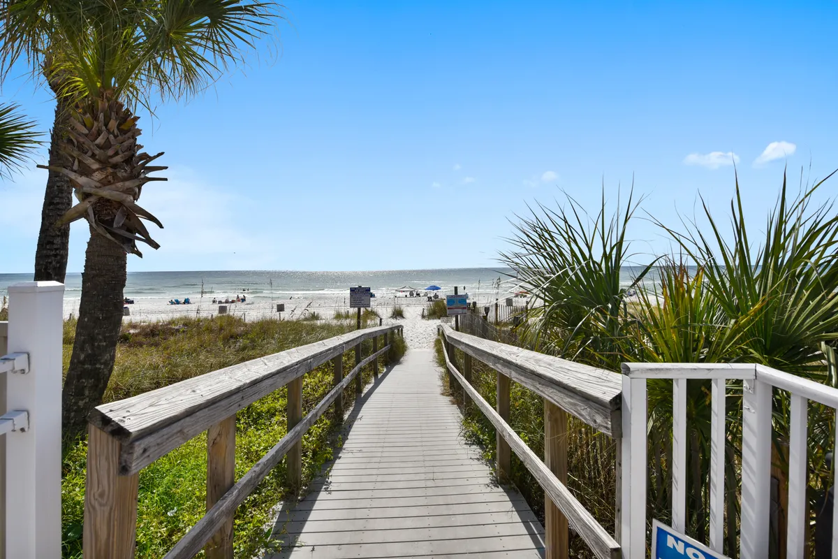 A wide wooden boardwalk stretches toward a pristine Gulf beach, lined by palm trees and opening up to soft sand and the sparkling ocean beyond. The area feels tranquil, welcoming, and perfect for family strolls. The expansive beach invites guests of all ages to relax, play, and take memorable family photos.