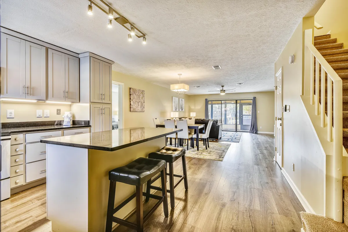 A bright, welcoming interior shot capturing the kitchen island, dining area, living area, and a staircase in a single open-plan space. The arrangement is ideal for hosting family gatherings, sharing meals, and socializing, illustrating how the space seamlessly accommodates multiple group activities.