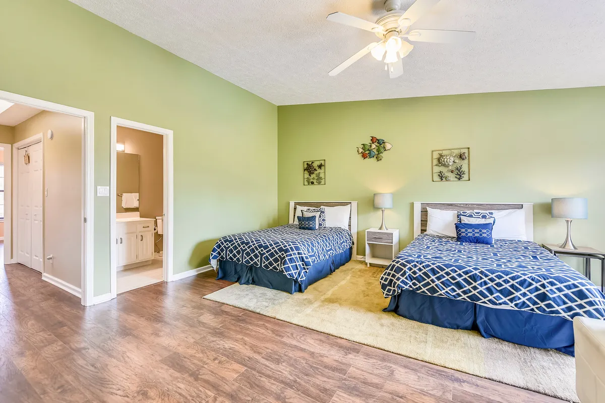 This cheerful bedroom shows two beds with blue and white bedding, accented by light green walls and decorative wall art. The setup is inviting for siblings or cousins, with an atmosphere of playful relaxation ideal for family gatherings or cozy evenings.