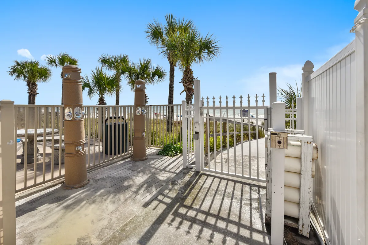 A welcoming gated resort entrance framed by palm trees with a clear pathway leading toward the beach. The secure, well-maintained grounds invite guests to explore and enjoy the nearby amenities.