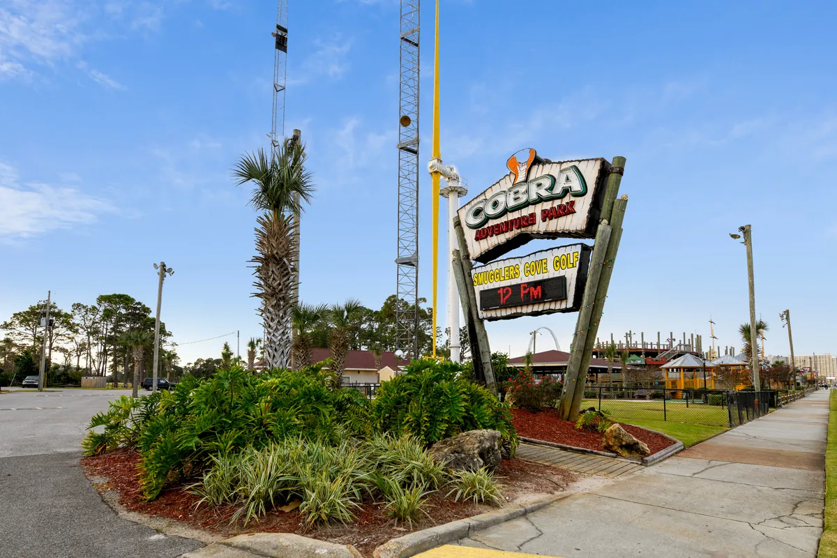 A playful exterior scene at Cobra Adventure Park, featuring a prominent sign, lush palm trees, and hints of mini-golf and playground equipment in the background. The mood is fun and energetic, suggesting friendly competitions and special family memories.