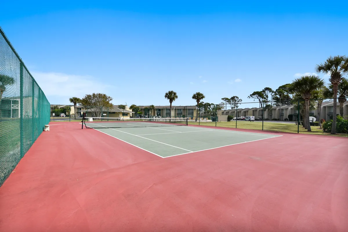 Sunny tennis courts bordered by green grass and palm trees, with residential resort buildings in the background. The space encourages social play, exercise, and casual gatherings—ideal for families and friends seeking active, outdoor fun.