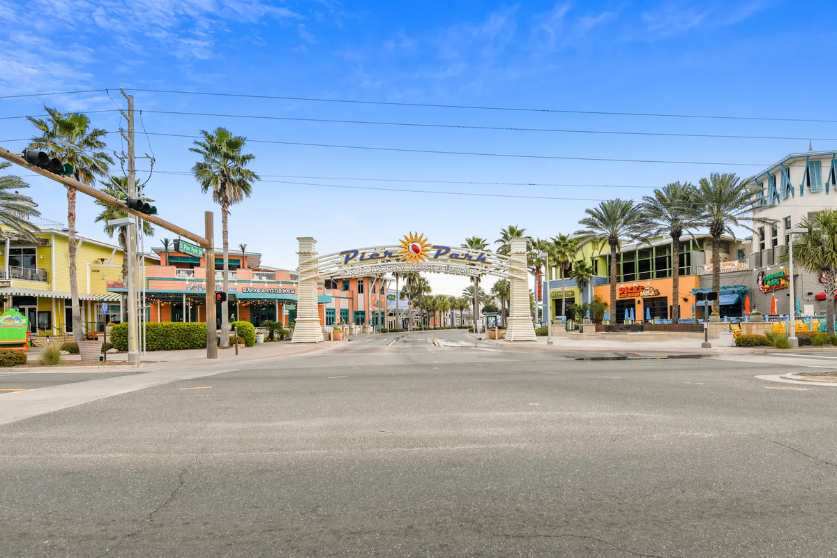 The entrance to Pier Park—a vibrant shopping, dining, and entertainment district—features a colorful archway, palm trees, wide pedestrian-friendly streets, and lively storefronts. The scene is bustling and inviting, reflecting the energy of Panama City Beach’s local attractions.